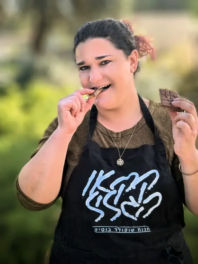 חנה קונינג, בעלת קקאו הגליל, טועמת שוקולד ומחזיקה טבלת שוקולד ביד